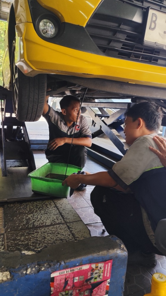 Montir mengganti oli mesin mobil